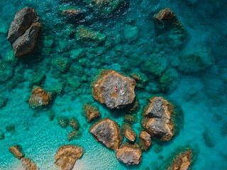 directly above woman in red swimsuit at the rock surrounded by the sea