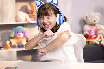 Fototapeta premium Happy cute small caucasian kid girl in headphones dancing and singing having fun in apartment. People, lifestyle and joy concept