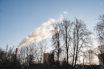 The city is polluted by harmful emissions coming out of the pipes of the plant. The carbon footprint falls on buildings, climate warming, a pipe against the sky.