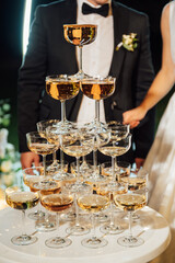 A large pyramid of champagne glasses at the evening ceremony at the arch. bride and groom are hugging