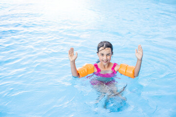 Fototapeta na wymiar happy little girl having fun in the pool in swimming suit.