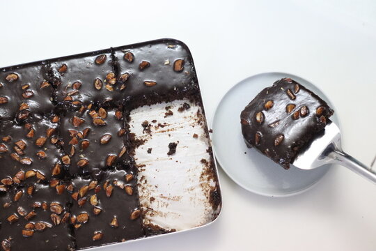 Slice of Texas sheet cake served on a plate. Buttery and chocolaty cake sliced to rectangular pieces inside the baking bin and scooped from it