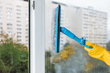 Man in yellow rubber gloves cleaning window with cleaner spray detergent and squeegee or rag at...