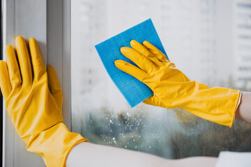 Man in yellow rubber gloves cleaning window with cleaner spray detergent and squeegee or rag at...