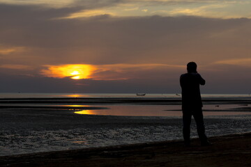Fototapeta na wymiar Photographer Silhouette is taking a sunset at the beach