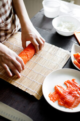 Young woman wrapping up sushi roll ingredients on bamboo mat.