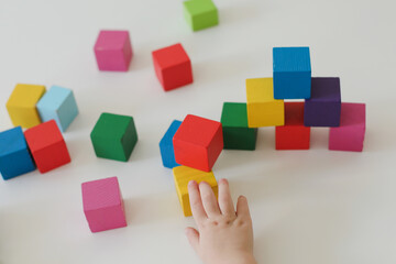 Top view child hands playing and building with colorful wooden toy bricks on white wooden table. Early learning and development