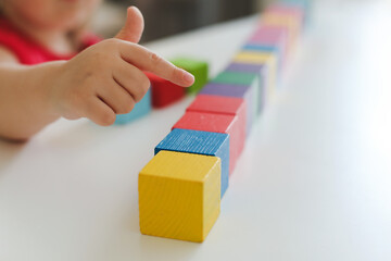  child playing and building with colorful wooden toy bricks on white wooden table. Early learning and development