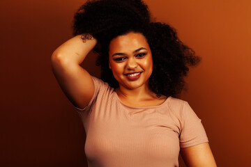 pretty young african american woman with curly hair posing cheerful gesturing on brown background, lifestyle people concept