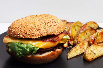 Vegan food. Close-up of homemade cheeseburger and baked potatoes on black plate.