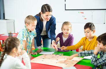 Happy kids and female teacher playing together educational board game in classroom at elementary...