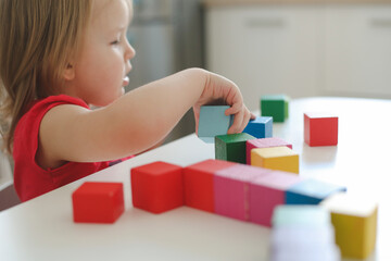  child playing and building with colorful wooden toy bricks on white wooden table. Early learning and development