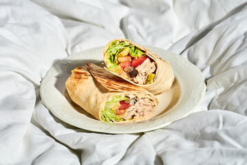 Shawarma with chicken and vegetables in a plate on a white sheet. Hard light.