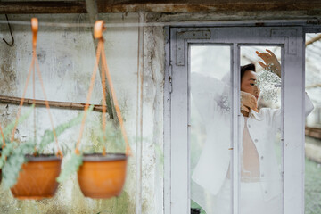 Obraz na płótnie Canvas Asian woman posing with flowers through window in greenhouse