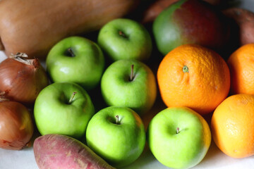 Green apples, oranges, mango, butternut squash, onion and sweet potato on the table. Selective focus.
