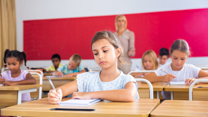 Fototapeta na wymiar Portrait of focused tween schoolgirl writing exercises in workbook in classroom during lesson
