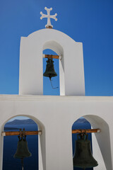 View of church bells and a crucifix at the top of a whitewashed church in Santorini