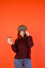 Business portrait of beautiful young woman with red curly hair and blue eyes against red background. Drinking coffee. Using mobile phone. 