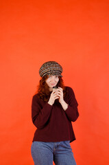 Business portrait of beautiful young woman with red curly hair and blue eyes against red background. Drinking coffee. Using mobile phone. Lifestyle.