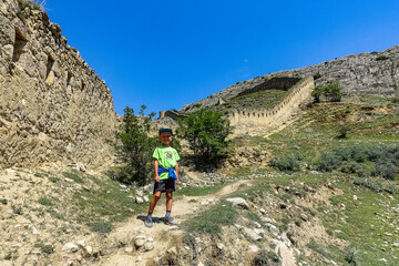 Fototapeta premium A boy against the background of the Gunib fortress. A protective wall. Russia, Dagestan. June 2021