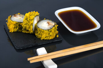 close-up, on a black table with a reflection, Japanese rolls with cream cheese and eel in tempura, next to a container with soy sauce and wooden sticks