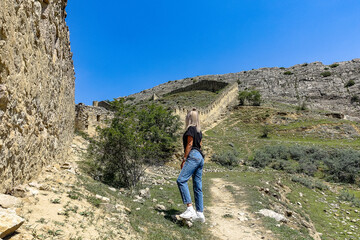 Fototapeta premium A girl against the background of the Gunib fortress. A protective wall. Russia, Dagestan. June 2021.