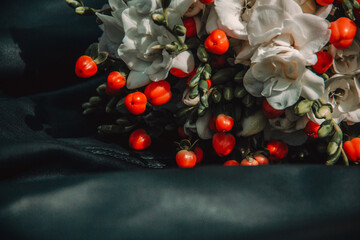 closeup wedding bouquet white flowers with red berries on the black leather jacket background at sunny day. decoration wedding concept, free space