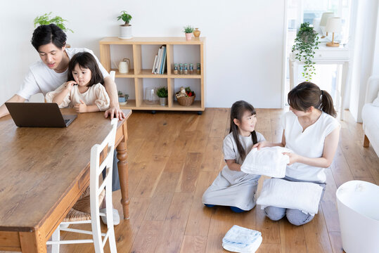 洗濯物を畳む母娘とパソコンを見る父子