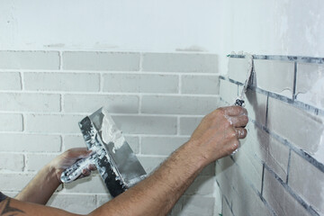 Close-up - a man's hand with a spatula applies plaster to the wall through a stencil in the corner...