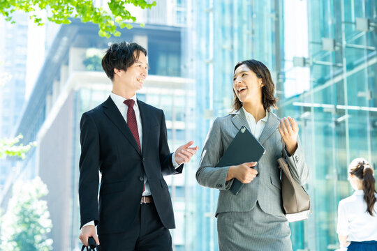 談笑しながらオフィス街を歩くスーツ姿の男女