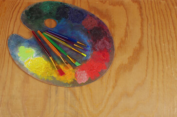Art palette with paints and artistic brushes on a wooden texture background. Copy space. 