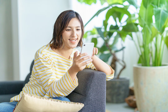 部屋でスマートフォンを操作する女性