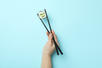 Female hand hold chopsticks with maki on blue background © Atlas