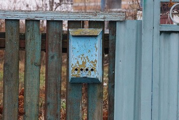 one old blue rusty metal mailbox hanging on gray wooden planks of a fence wall in a rural street