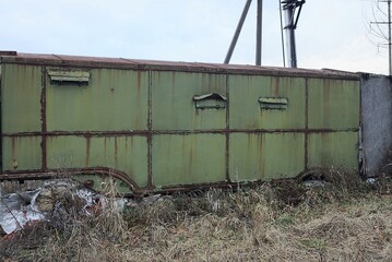 one old green iron trailer stands in dry gray grass and vegetation in the street 