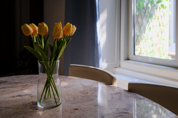yellow tulips in vase on the table. flowers in home interior and natural light