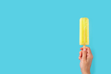Hand holding a lemon popsicle on blue background. Copy space