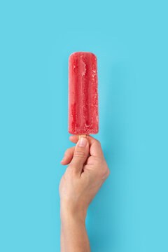 Hand holding a strawberry popsicle on blue background