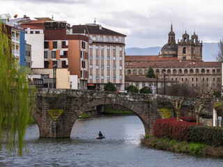 Fototapeta premium A canoeist sailing surrounded by ducks on the waters of the river Cabe under a Roman stone bridge and the Nuestra Señora de la Antigua school in the background