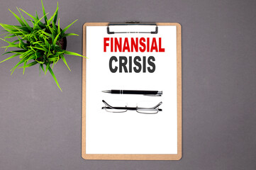 Text FINANCIAL CRISIS on the brown clipboard on the grey background. Business concept