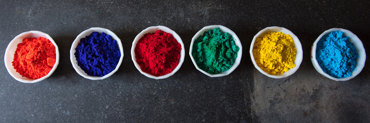 Gulal or holi festival powder colors in bowls on a dark background.