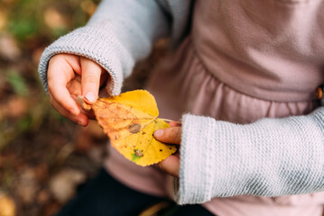 kleines Mädchen hält ein gelbes Herbstblatt in den Händen horizontal