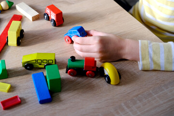 Fototapeta premium close-up of child's hands holding colored wooden cubes, dominoes, child 7-9 years old builds houses, rolls cars, concept of construction game, development of creativity, fine motor skills, patience