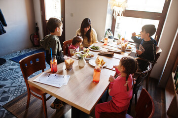 Mother with four kids spending time in cafe. Family lunch in the cafeteria.