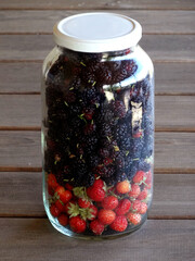 Strawberries and black mulberries on a glass jar.     