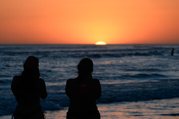 Silhouettes of two people watching a colorful sunset on the beach.