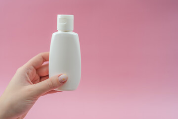 Woman's hand holds white plastic tubes on pink background. Сosmetic bottles for beauty or medicine products