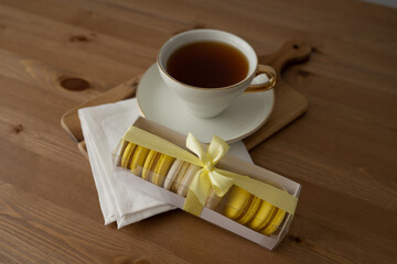 Yellow French macaroons in a beautiful white box, a cup of tea. Sweet dessert for tea. Gift box of macaroons with a beautiful satin ribbon.