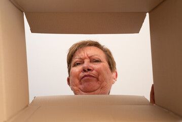 Face of a senior woman looking inside a open package with a disappointment gesture due to a wrong...