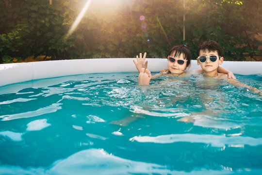 Two kids boy and girl swim in inflatable circle pool on summer sunny day outdoors. Children wear sunglasses. Summer vacation and healthy lifestyle concept. Copy space. Wide angle shooting.